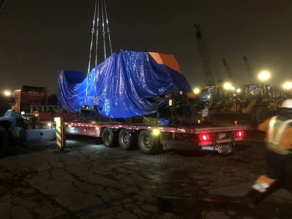 A covered Qingwei tube bundle extractor being unloaded from a flatbed trailer by crane at night